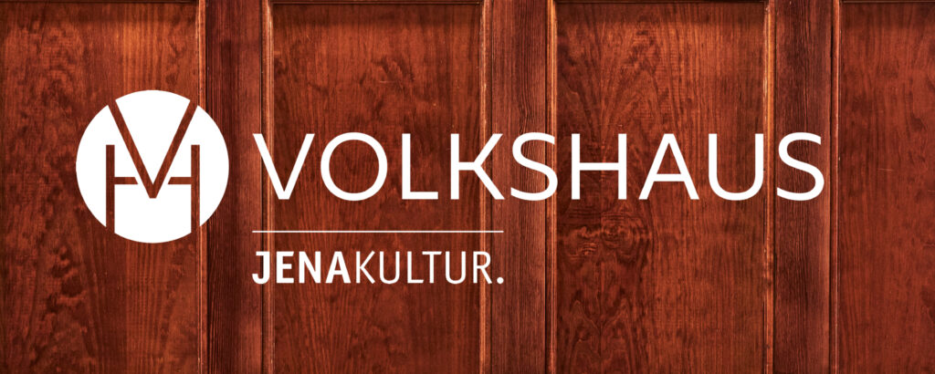 horizontales, weiĂźes Volkshaus-Logo mit einem den Initialien der Einrichtung zusammengefassten Emblem auf einer einem Foto, das Holzpanele darstellt